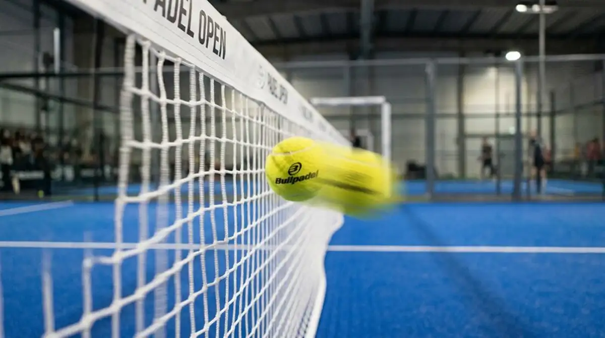 Pallina da padel che attraversa la rete dopo un servizio vincente, in primo piano sulla traiettoria