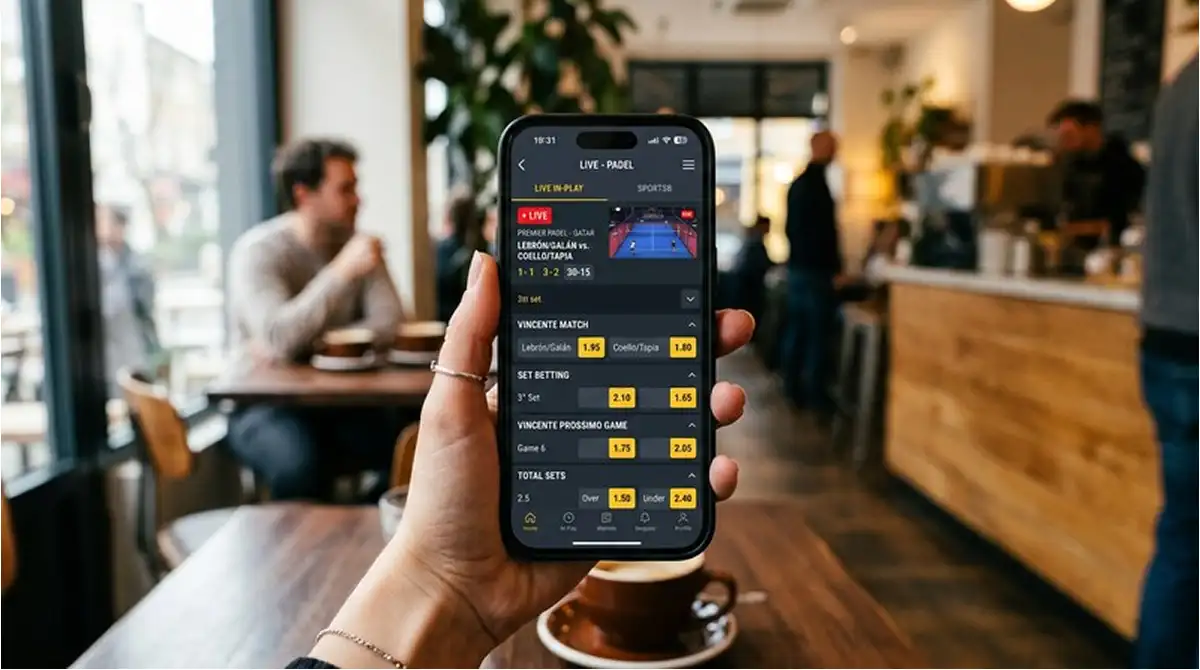Mano che tiene uno smartphone con l'app di un bookmaker ADM aperta sul palinsesto live padel durante un match